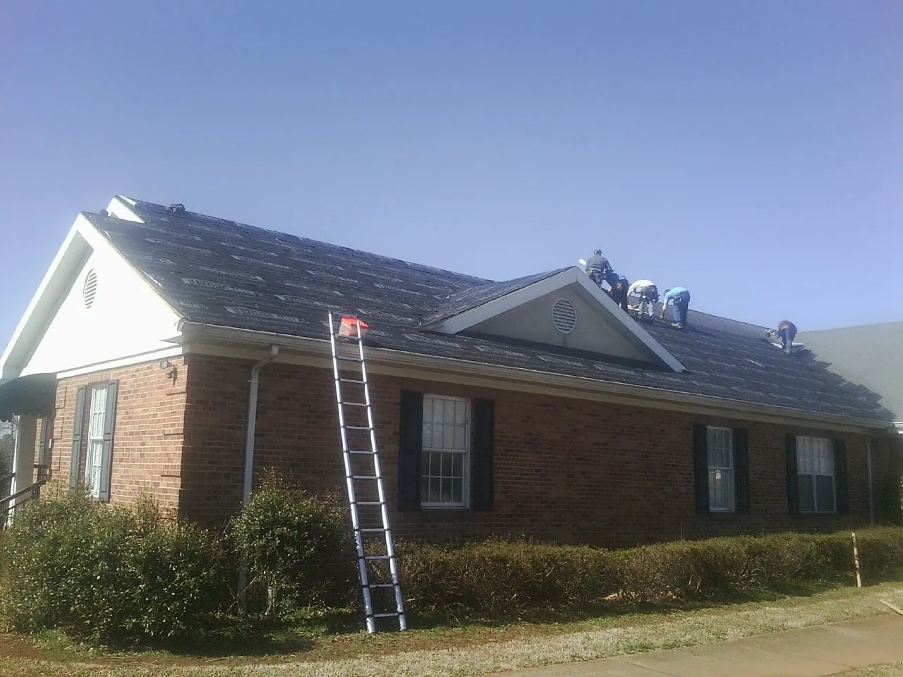 Crew tearing shingles off a brick ranch roof with a ladder set — Emergency Roof Repair work by our crew in Offutt Afb