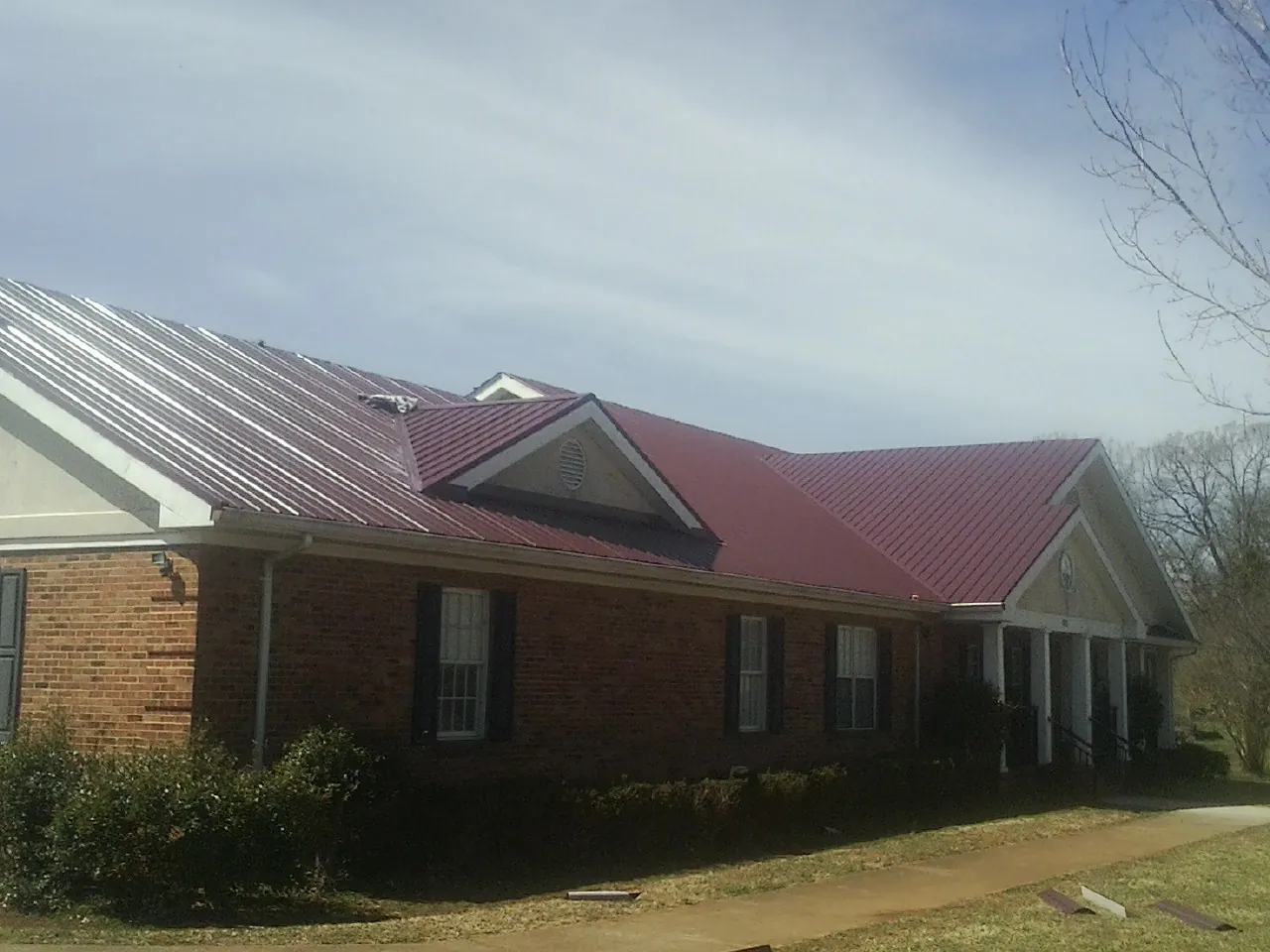 Red metal roof with gabled entries on a long brick building, from a Hail Damage Roof Repair job in Offutt Afb