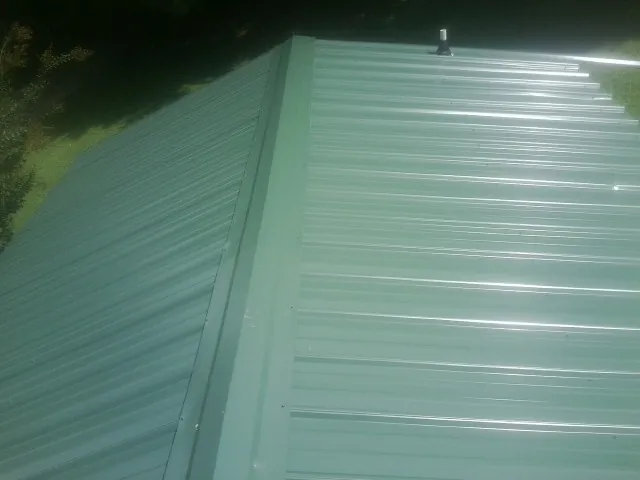 New green metal panels meeting at the ridge of a roof — Flat Roof Repair work by our crew in Offutt Afb