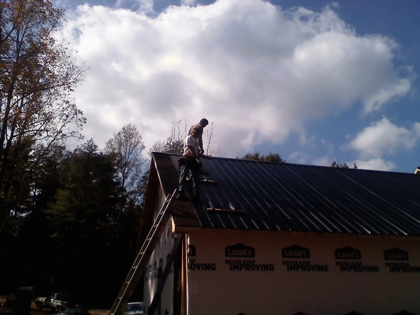 Roofer fastening dark metal panels high against a cloudy sky, from a Roof Inspection job in Offutt Afb