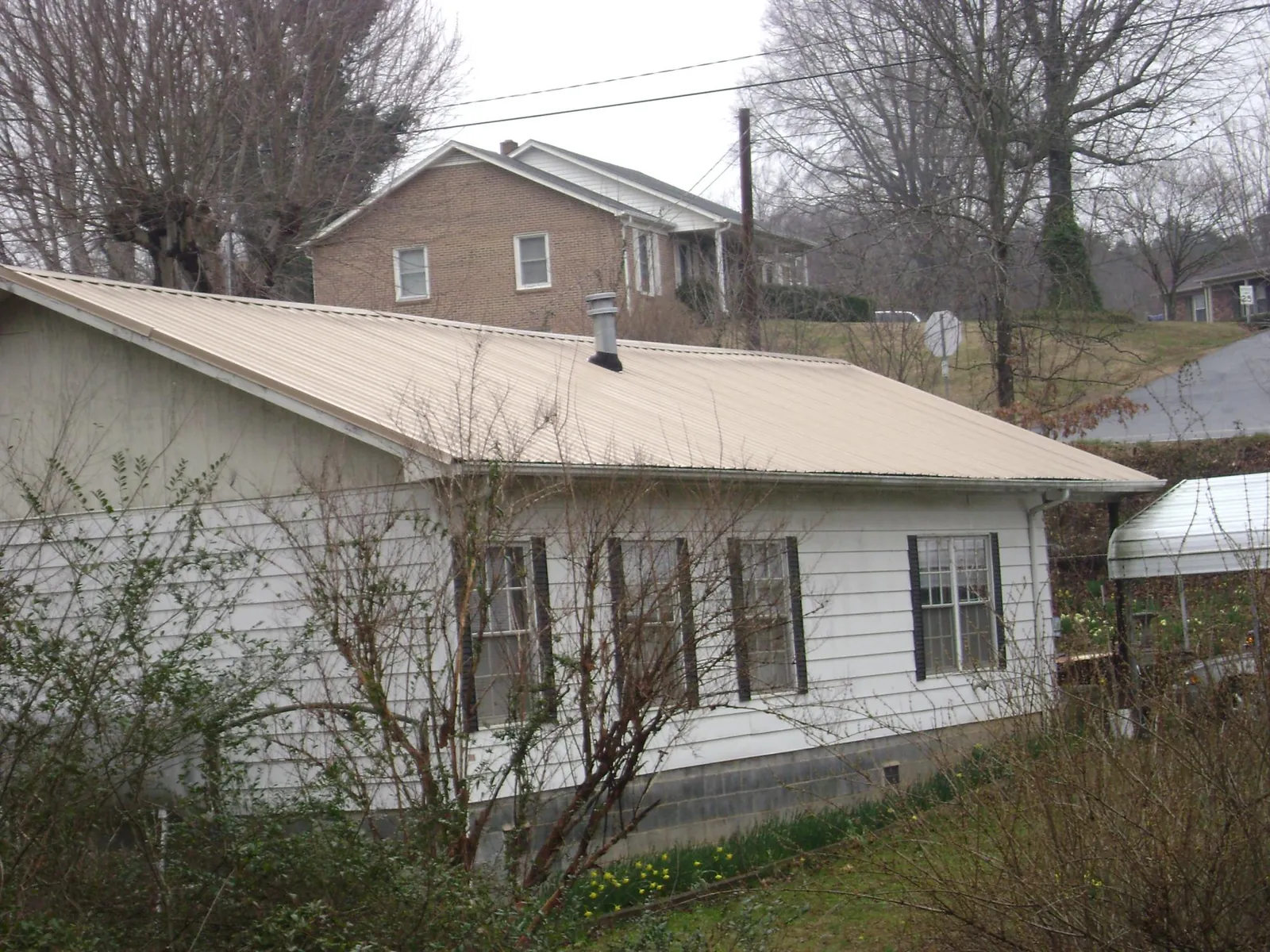 Tan metal roof on a white sided house set into a hillside — Commercial Roofing by Roofing Brothers in Offutt Afb